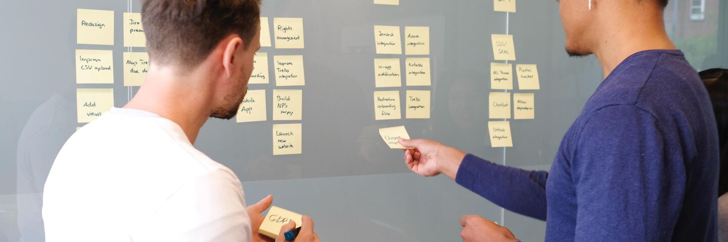 2 people brainstorm their campaigns with sticky notes on glass manifestations in the office