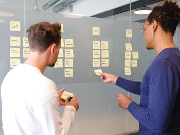 2 people brainstorm their campaigns with sticky notes on glass manifestations in the office