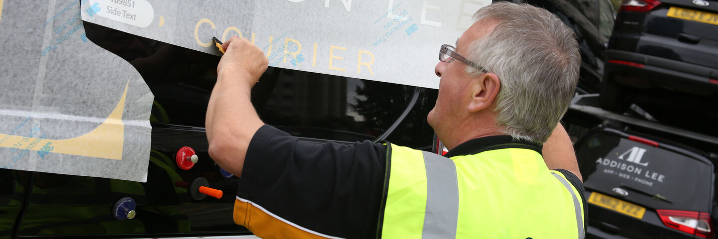 Man applying branded graphics onto Addison Lee vehicle
